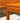 Close-up of a wooden table corner with smooth, rounded edges and visible grain, reflecting mid-century craft. In the blurred background is a Rare set of Alpa Teak Nesting Tables – Set of 3 - Australian Mid-Century Modern (Revive).