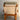 A Tessa Monaco Armchair – Sage Green Like New (Revive) with a wooden frame, light beige fabric backrest, and green cushioned headrest featuring leather accents sits on a smooth concrete floor against a plain light grey wall.