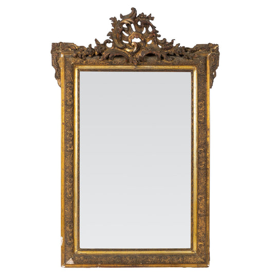 Ornately carved giltwood Louis XV-style mirror with Rococo detailing and a dramatic crest with intricate detailing throughout the frame. Found in Provence