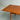 A close-up of the Fully Restored Parker 140 Square Extension Table (Rediscover) showcases its rich brown teak finish, clean lines, and visible wood grain, standing on tapered legs against a light gray wall and concrete floor.