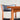 A close-up of a mid-century modern wooden chair with a black seat and backrest, placed behind the Fully Restored Parker 140 Square Extension Table (Rediscover) against a plain light-colored wall.