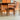 Four fully restored Parker T-Back Number 88 dining chairs in terracotta surround a matching wooden dining table on a concrete floor, with a wooden cabinet and glass display case visible in the background.