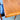 A close-up of the Vintage Parker Dining Suite 5 Piece Square - Number 140 shows a wooden table corner with visible grain and a rounded edge; a black cushioned chair is partially tucked under the table on the left.